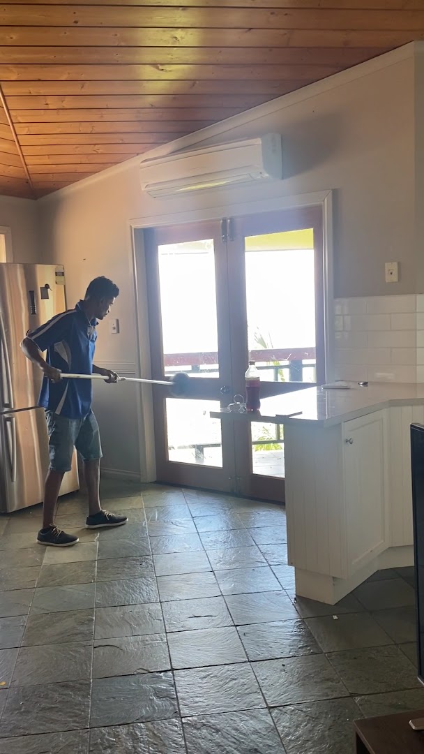 A cleaner working a long-handled mop across a slate tiled floor in an open living area