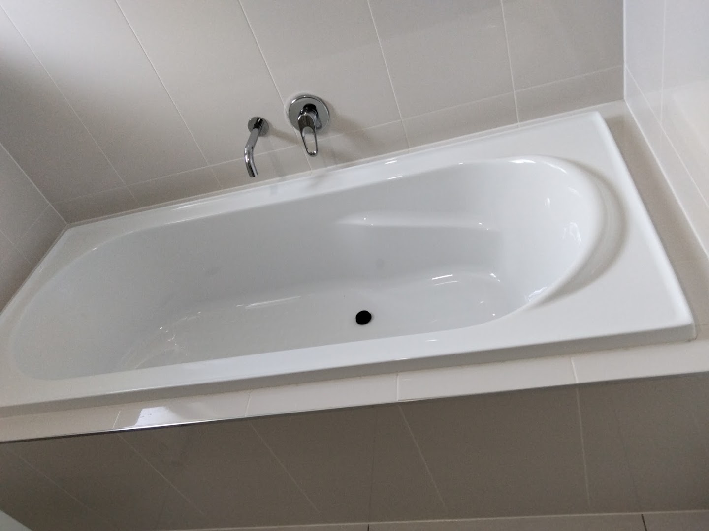 A white bath set into a tiled bathroom with the wall mixer above it