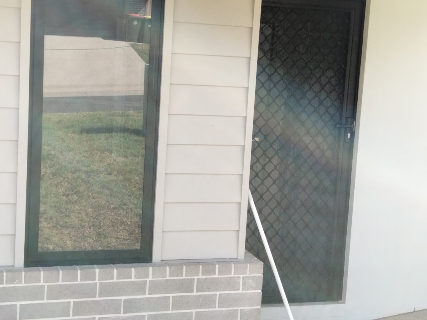 Windows and a screen door on a weatherboard and brick wall with lawn beyond