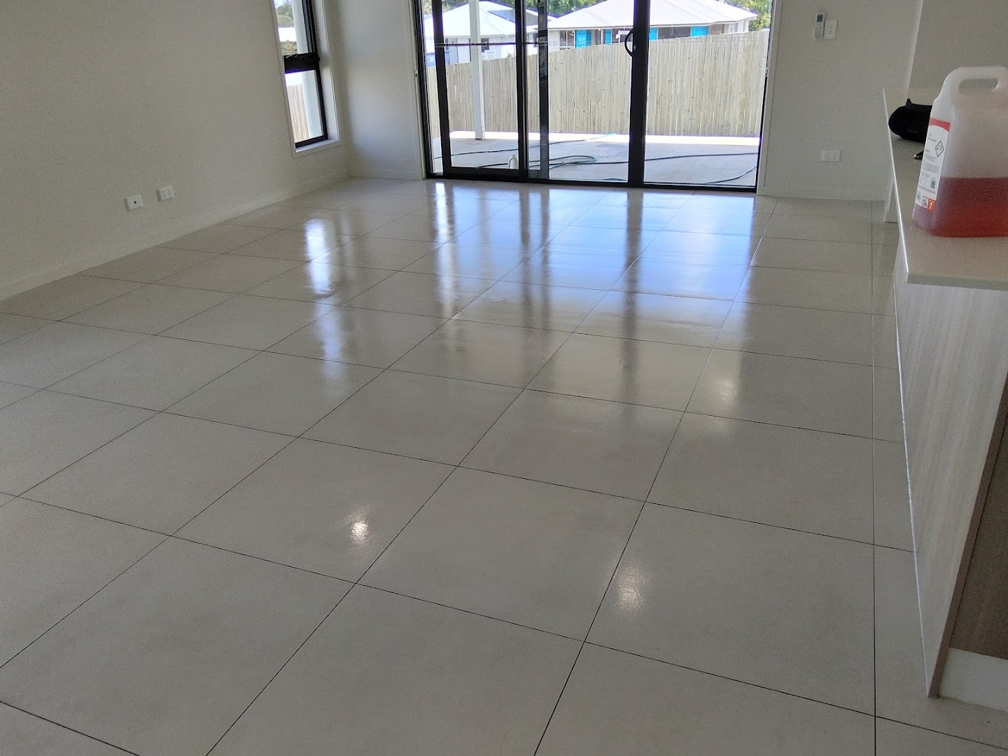 An empty open-plan living area with a large-format tiled floor and glass sliding doors