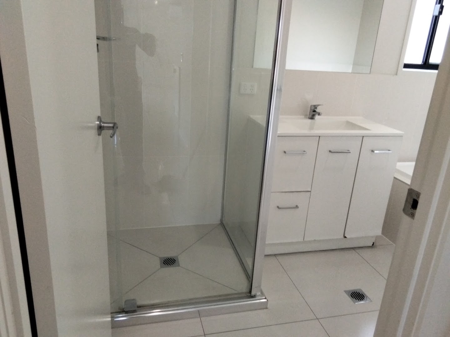A glass shower screen and a white vanity in a tiled bathroom