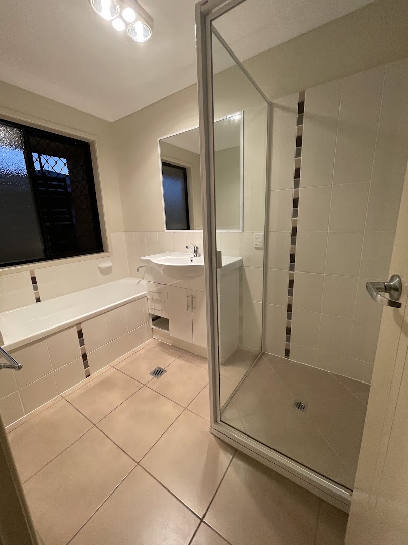 A bathroom with a bath, a glass shower screen and a tiled floor
