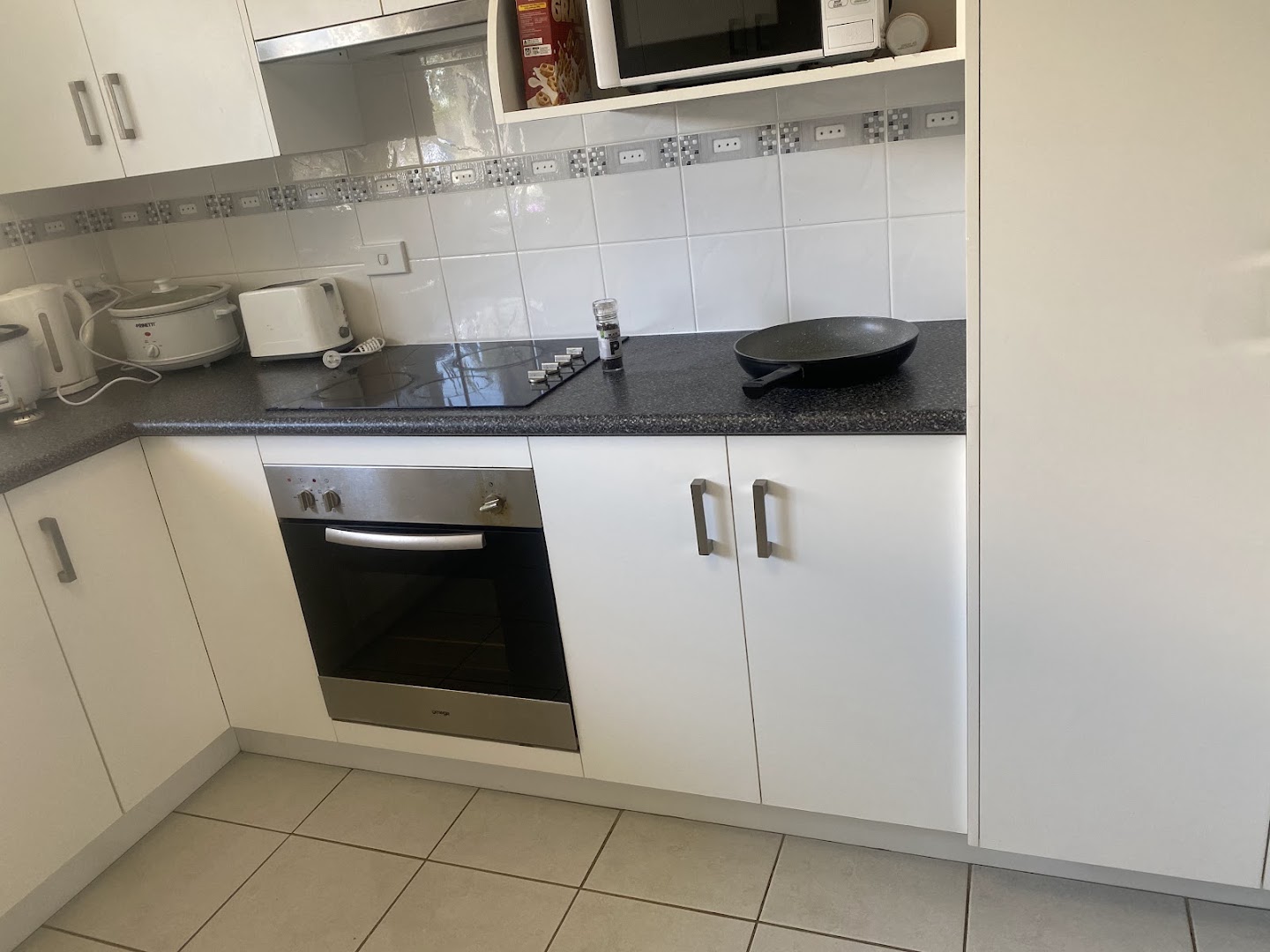 A kitchen with a wall oven, glass cooktop and tiled floor