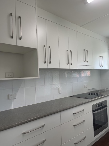 A white kitchen with overhead cupboards, a stone benchtop and a tiled splashback