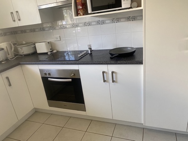 A kitchen with a wall oven, a glass cooktop and a tiled floor
