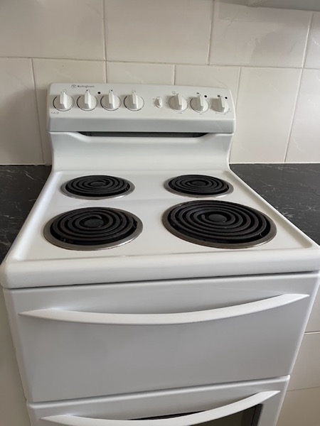 A freestanding white stove with four elements beside a dark benchtop