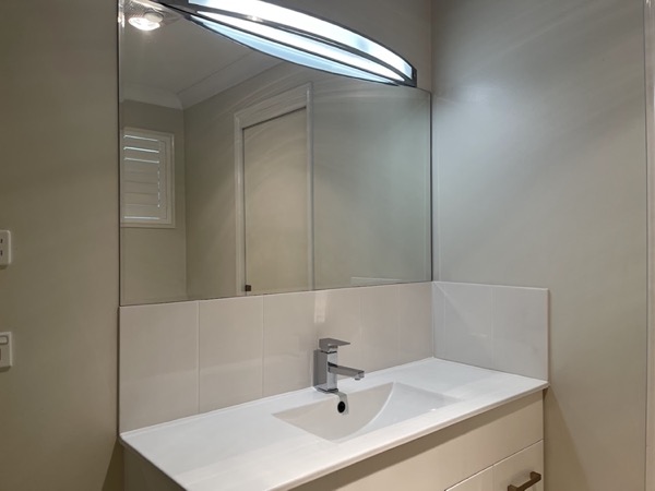 A bathroom vanity under a wide mirror with a tiled splashback