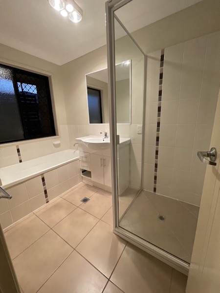 A bathroom with a bath, a glass shower screen and a tiled floor