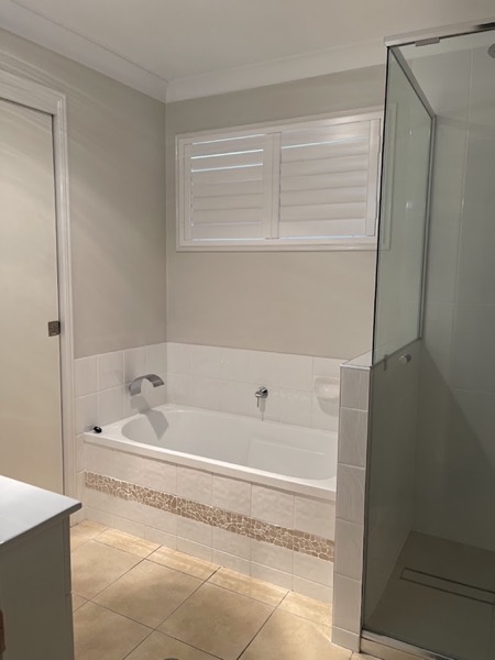 A bath beside a glass shower screen with a shuttered window