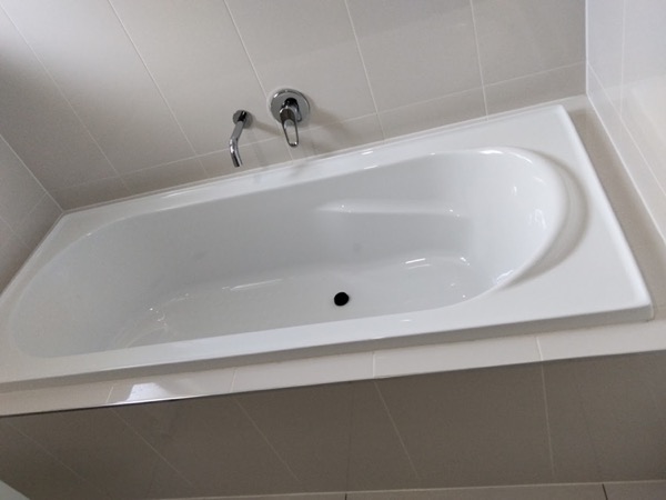 A white bath set into a tiled bathroom with the wall mixer above it
