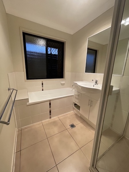 A bathroom with a bath, a shower screen and a tiled floor by a window