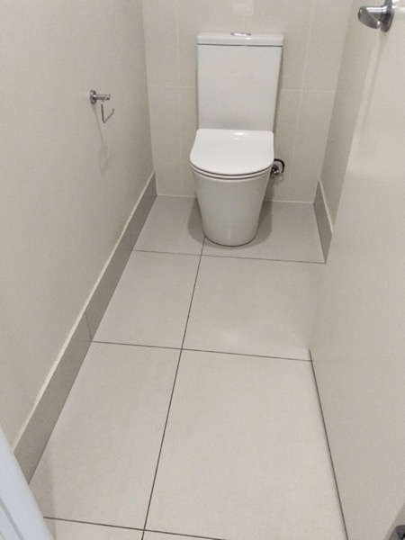 A tiled toilet room with a white pan and a paper holder