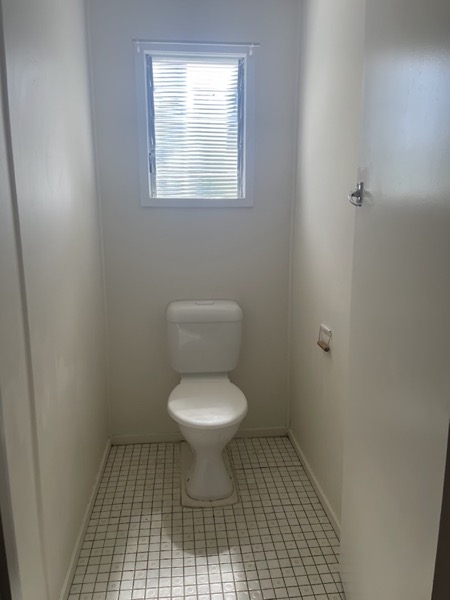 A toilet room with a small louvre window and a tiled floor