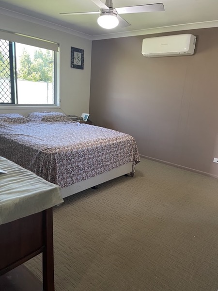 A carpeted bedroom with a bed, a window and a wall-mounted air conditioner