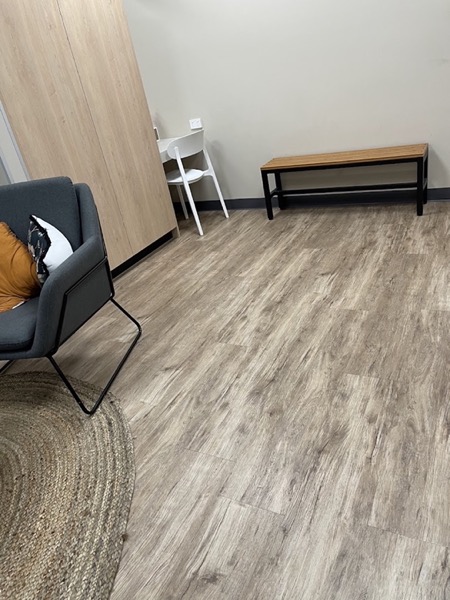 An empty room with a plank floor and a single armchair by the window