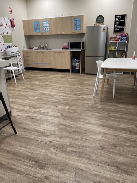 A staff room with a plank floor, a kitchenette, tables and chairs