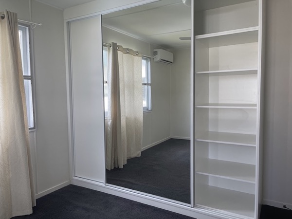 A bedroom with a mirrored sliding robe and open shelving