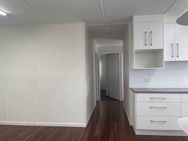 A white kitchen opening onto a hallway with polished timber boards