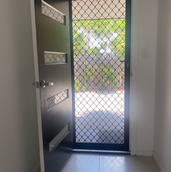 An open front door with a security screen and a diamond grille