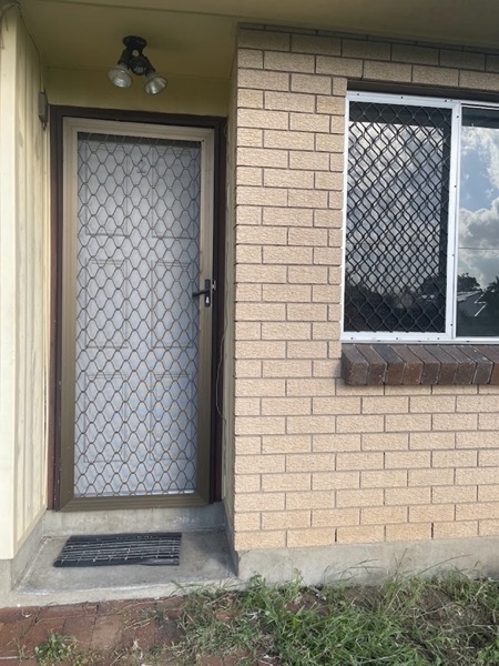 A brick entry with a security screen door and a window beside it