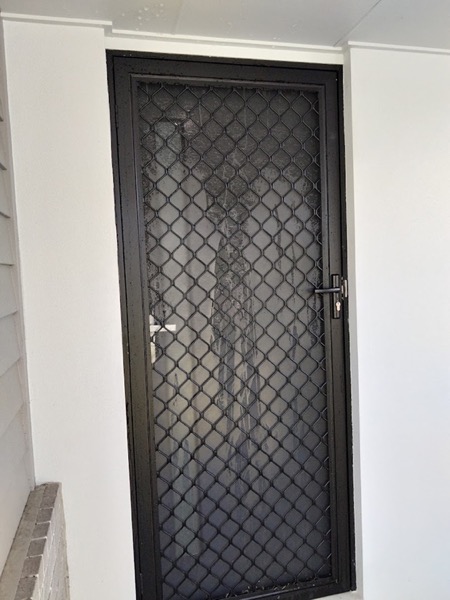 A security screen door with a diamond grille set in a white wall
