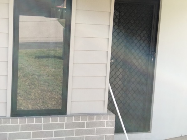Windows and a screen door on a weatherboard and brick wall