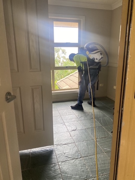 A cleaner working by a window with a backpack unit on a tiled floor
