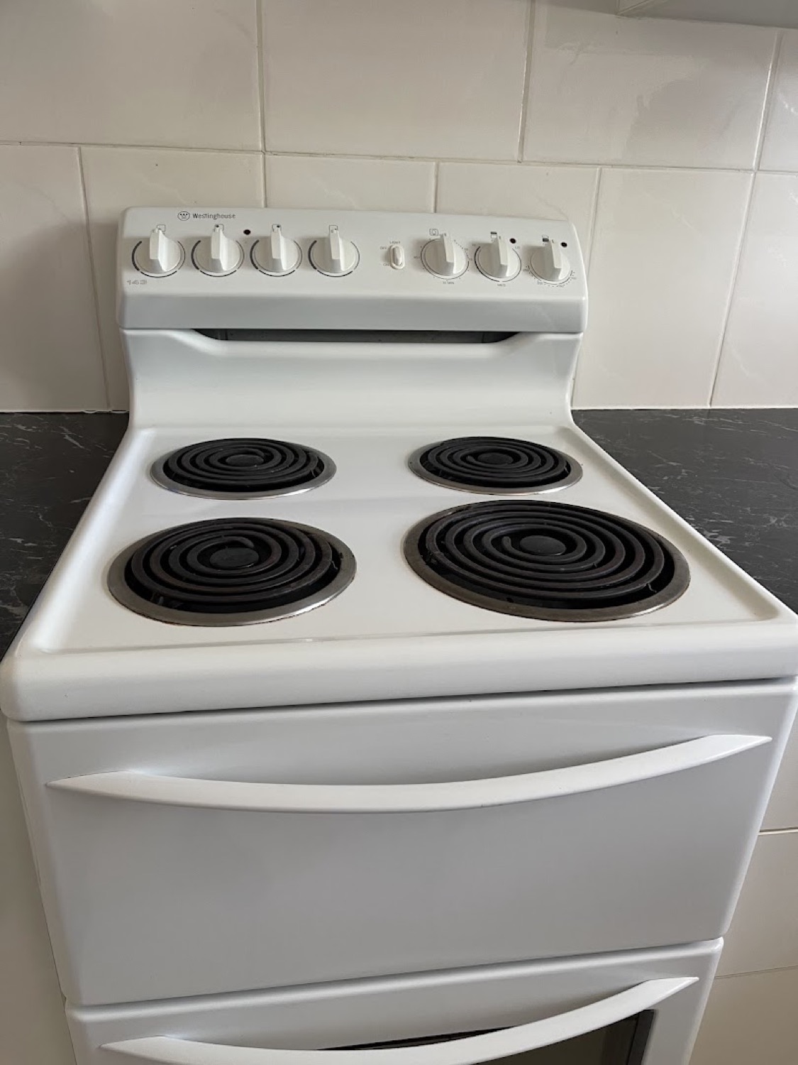 A freestanding white stove with four elements beside a dark benchtop