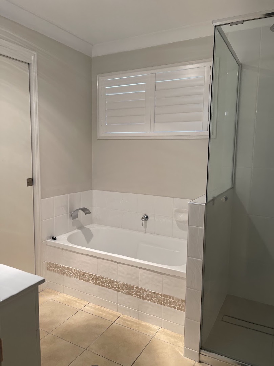 A bath beside a glass shower screen with a shuttered window