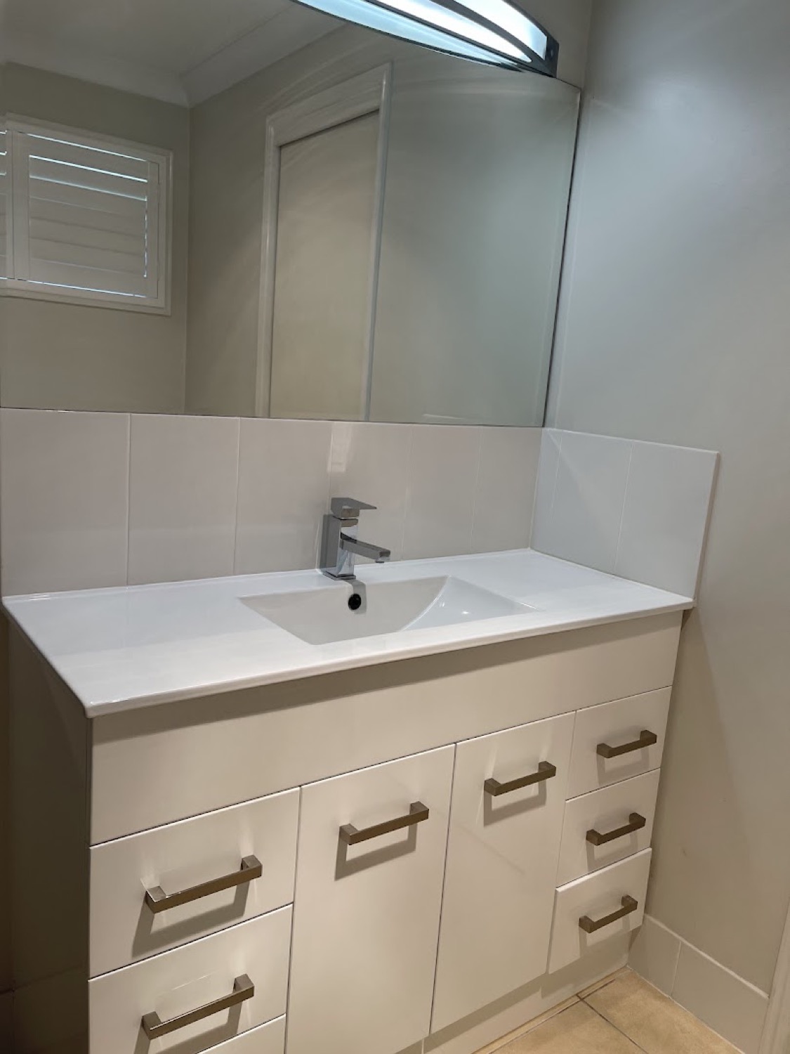 A bathroom vanity with a wide mirror and tiled splashback