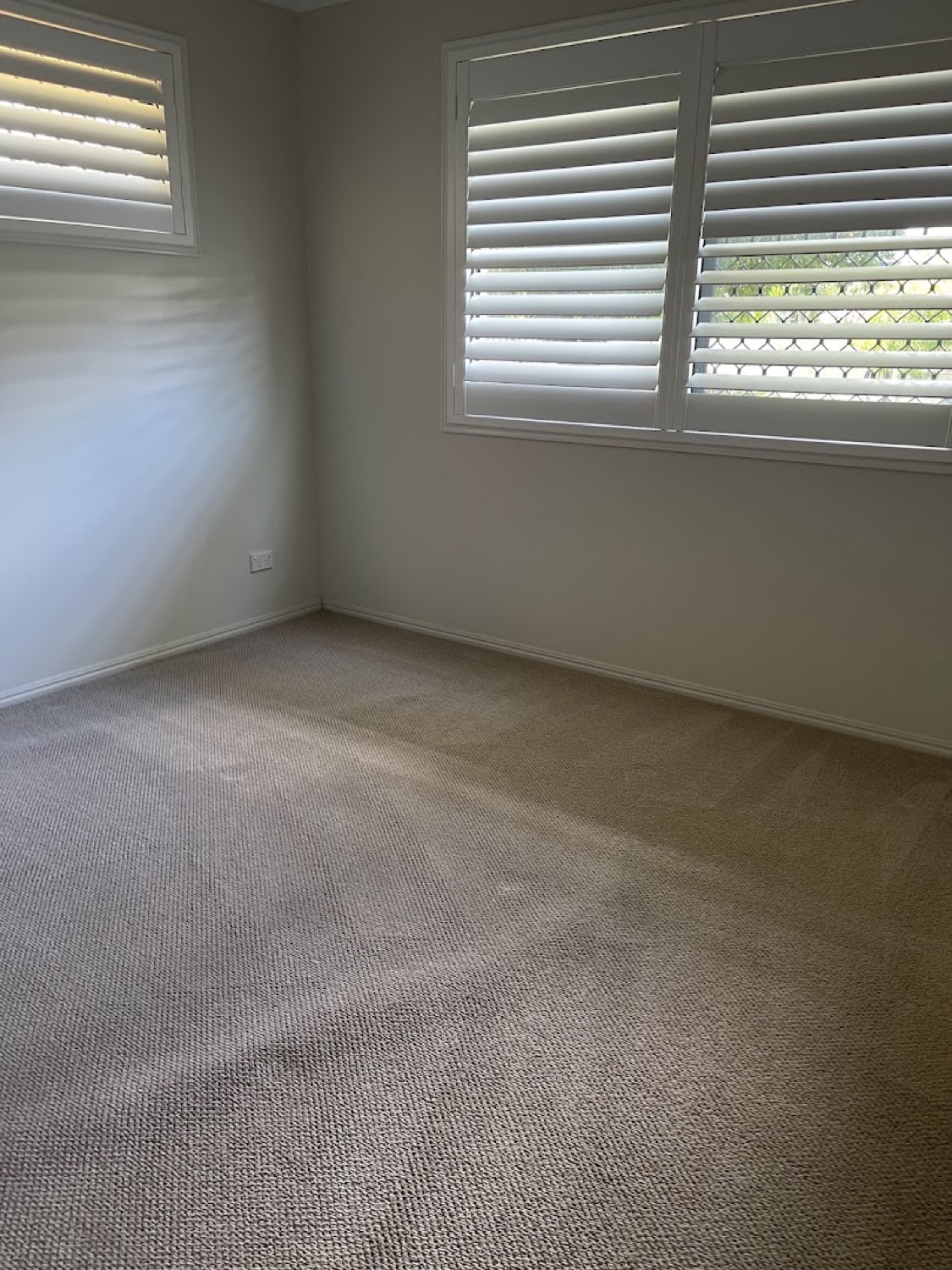 A carpeted room with louvre shutters on the window