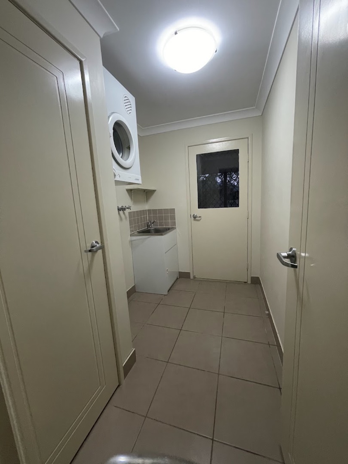 A hallway with a tiled floor and a laundry through the doorway